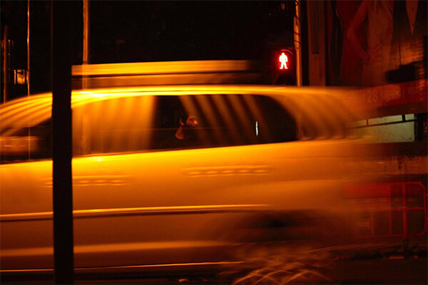 A car passes by as the photograph's subject waiting to cross the road