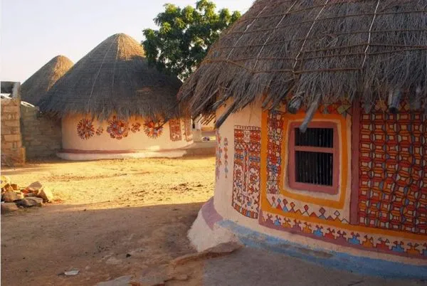 Traditional Rajasthani mud huts with intricate wall paintings and thatched roofs in a rural village setting.