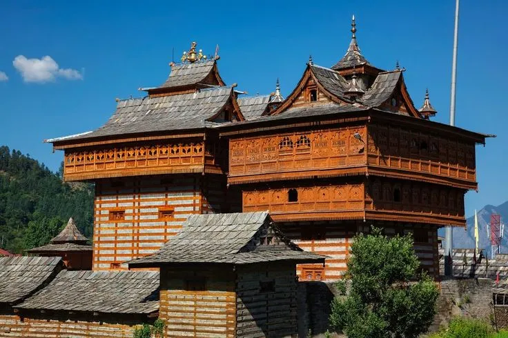 Ancient Himachali temple with wooden carvings and pagoda-style rooftops set against a mountainous backdrop.