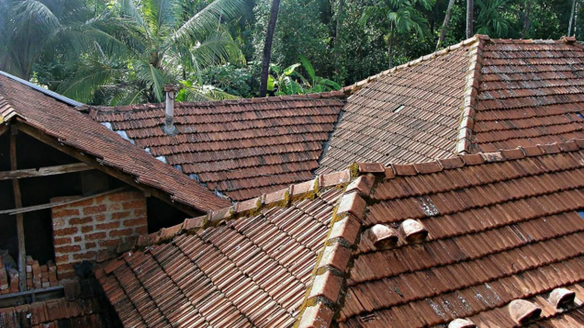 Traditional clay tiled sloping roofs of a Kerala house surrounded by lush greenery