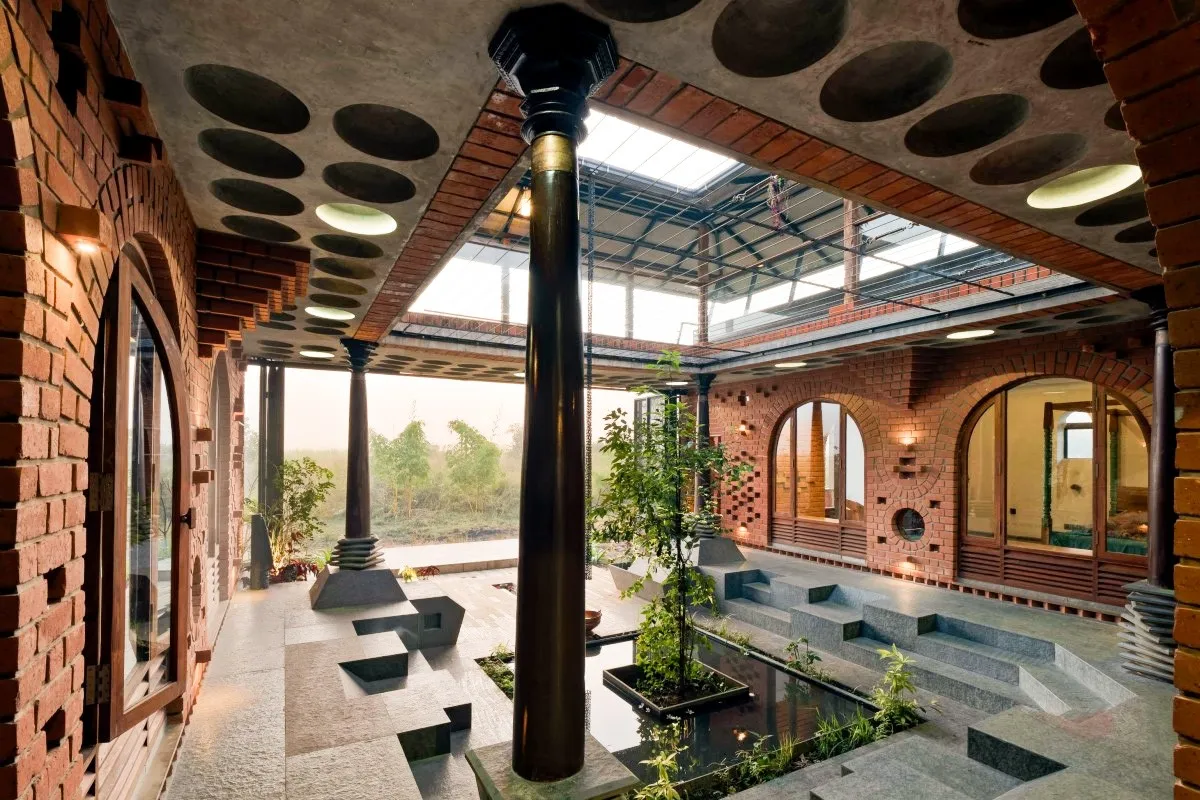 Modern Indian courtyard house with exposed brick walls, skylight roof, and central water feature promoting sustainable architecture.
