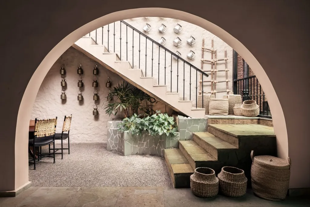 Rustic indoor courtyard with arched entryway, stone staircase, woven baskets, indoor plants, and traditional wall decor.
